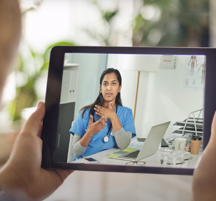 Tablet being held with medical professional on tablet screen talking to the person holding the tablet.
