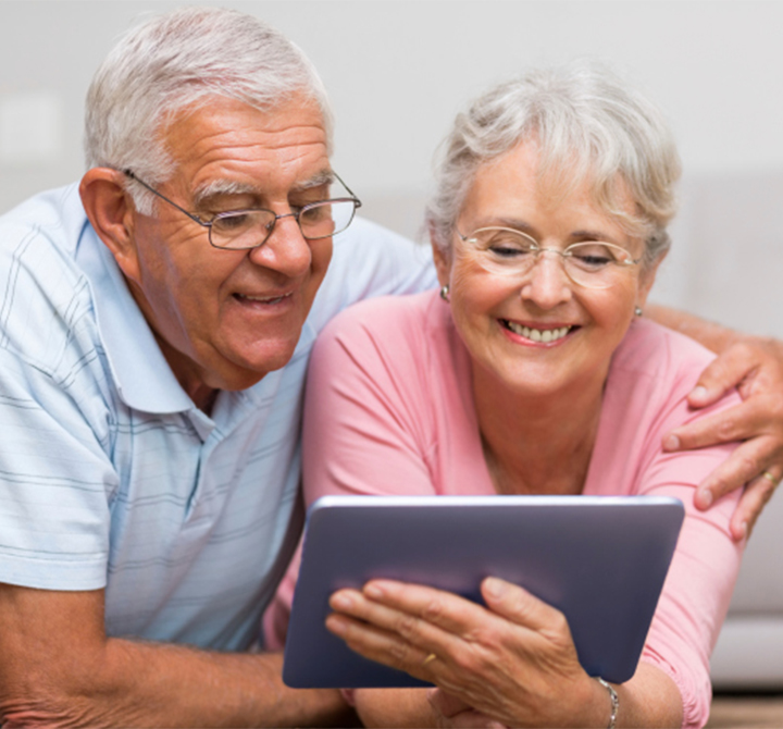 An older couple sharing a tablet and smiling. 