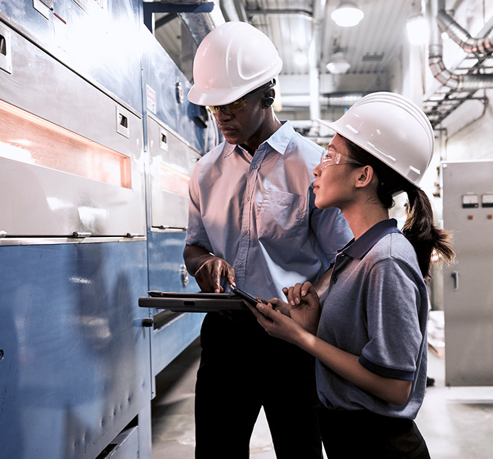 Man and woman wearing hardhats holding a tablet.