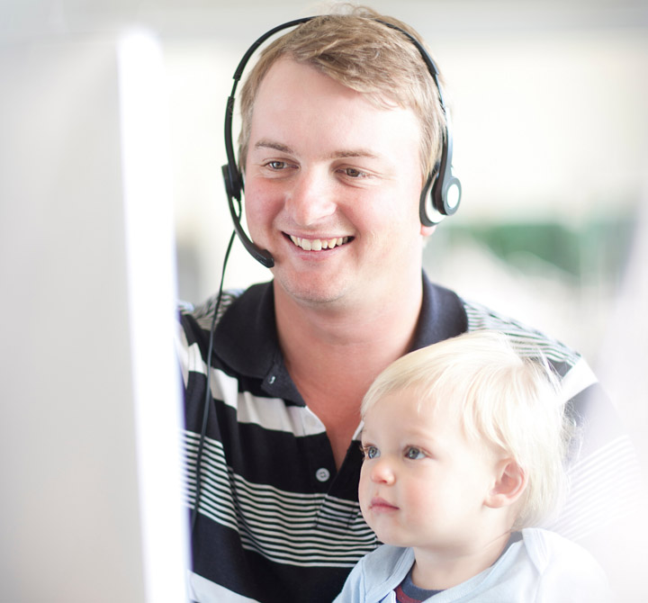 Man with headset on and child looking at computer monitor.