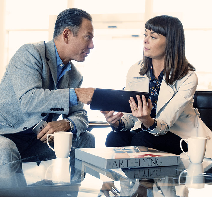 Business man and woman with coffee sharing a tablet and looking at each other. 