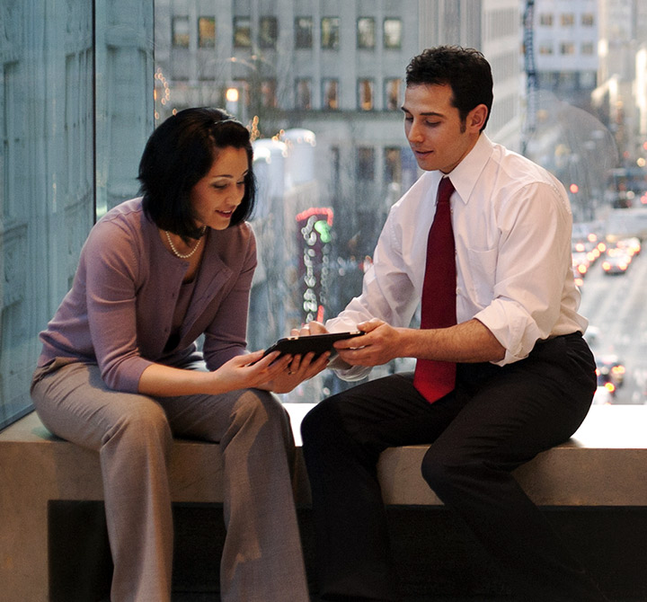 Man and woman in business attire both looking at a shared tablet. 