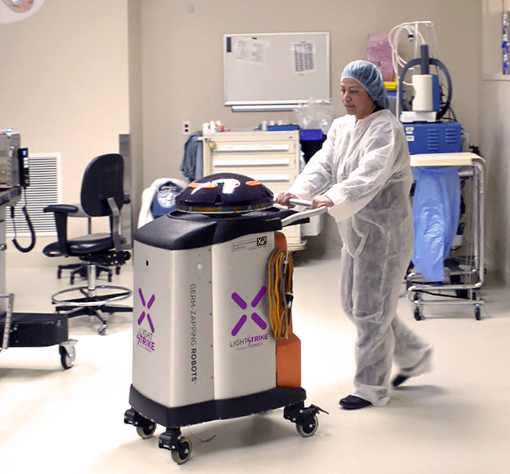 Nurse in medical scrubs pushing a Xenex machine. 