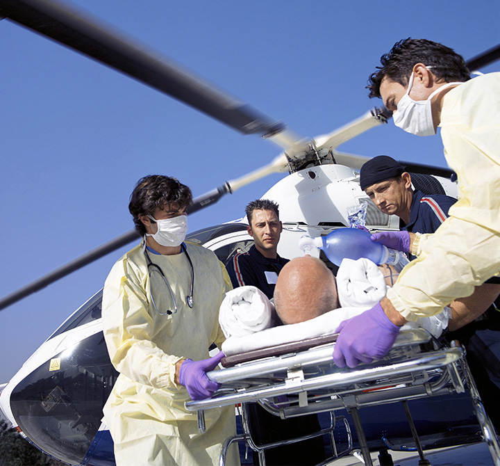 A medical helicopter in the background with doctors and EMTs pushing a man on a gurney.