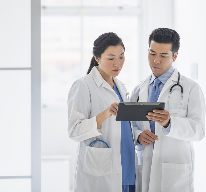 Two doctors in white lab coats sharing a tablet and looking at the screen.