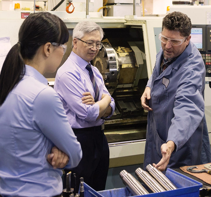 Three engineers looking at and discussing machine parts.