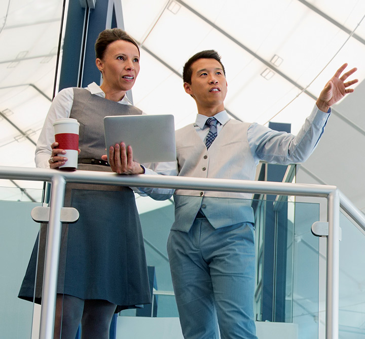 Male and female office employees on stairwell talking while holding a tablet.