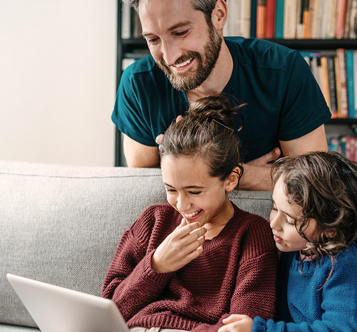 Family smiling on the couch while all looking at a laptop screen.