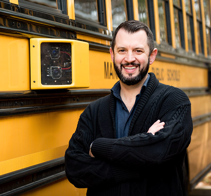 School bus driver standing in front of yellow school bus.