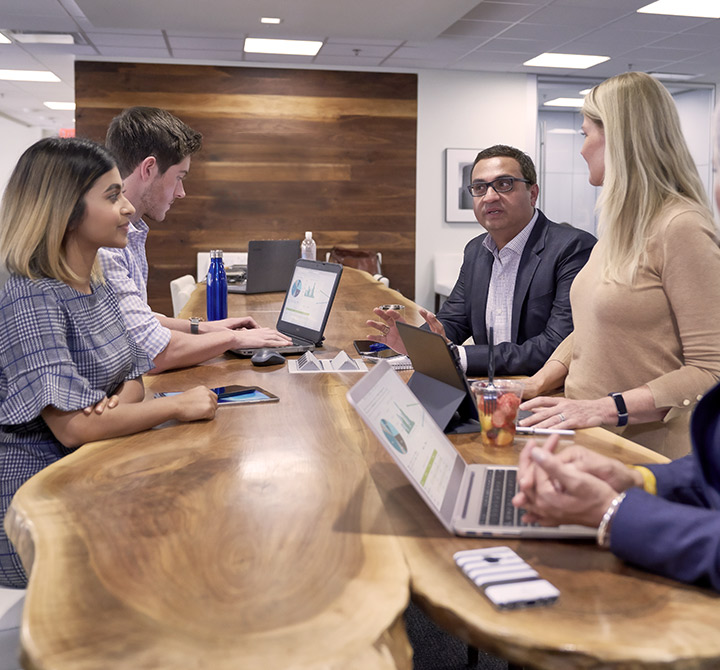 Group of office workers with computers at shared table talking.