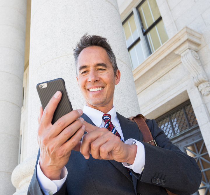 Man in suit looking at smartphone out in front of white pillar. 