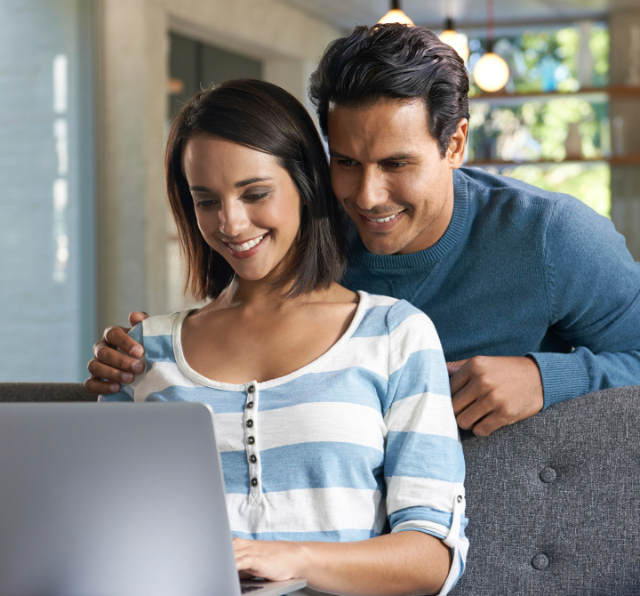Man and woman smiling while looking at a laptop screen.