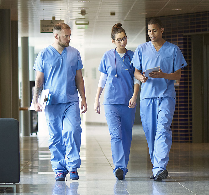 Three healthcare staff walking down a hallway in scrubs looking at a tablet. 