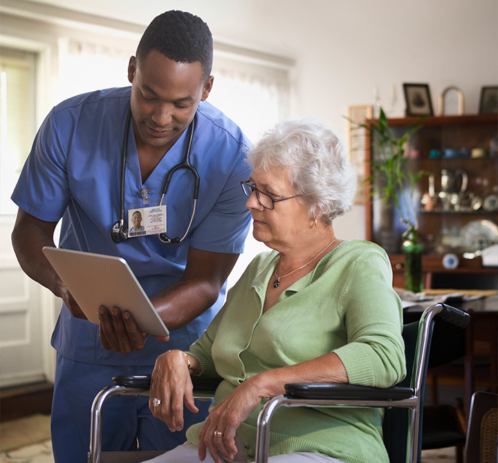 Male healthcare worker holding a tablet discussing results with a home patient in a wheelchair.