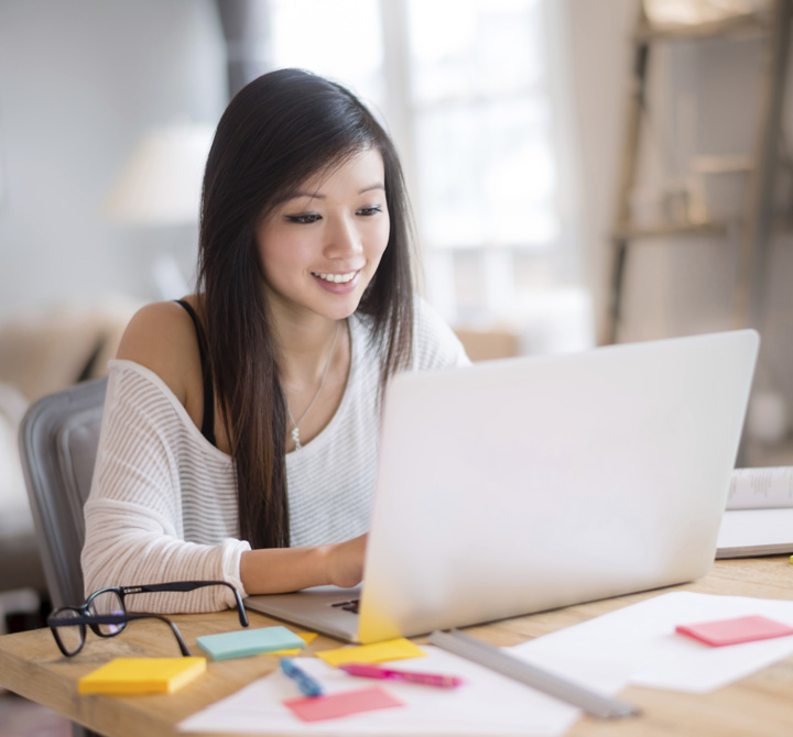 Woman on laptop with papers and post-its scattered around the desk. 