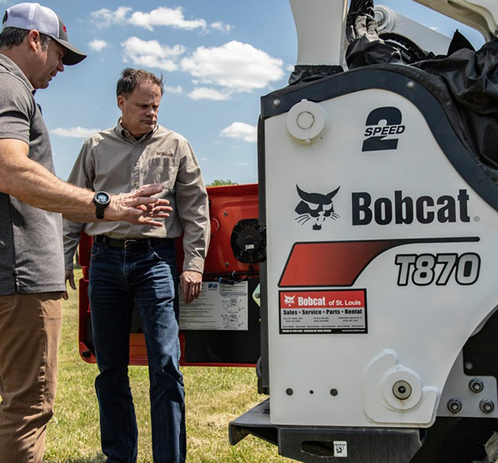 Two men standing by a Bobcat T870.