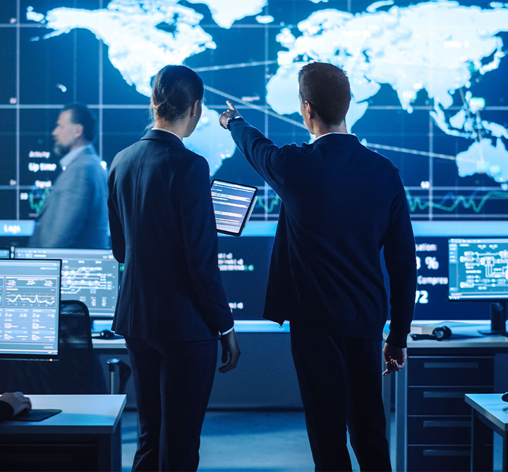 Man pointing at large screen while talking to woman in Security Operations Center.