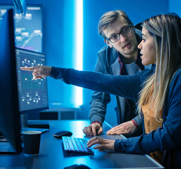 Woman pointing at computer monitor while talking to man.