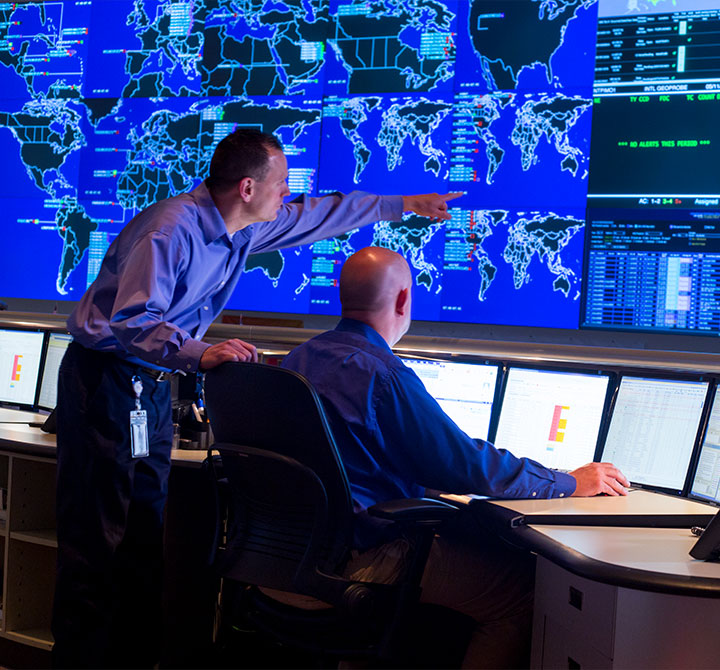 Man pointing at large screen while talking to another man in a Security Operations Center.