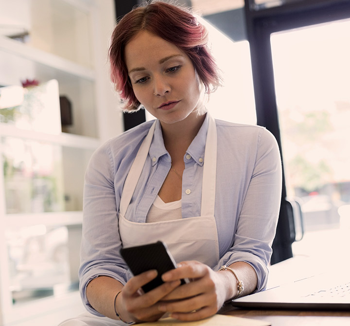 A female small business worker wearing an apron looking at her smartphone.