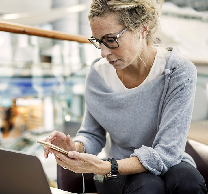 Woman working on smartphone connected to laptop.