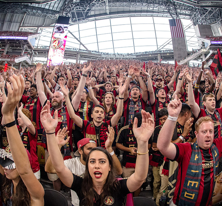 Atlanta Falcons fans in a stadium with arms up cheering