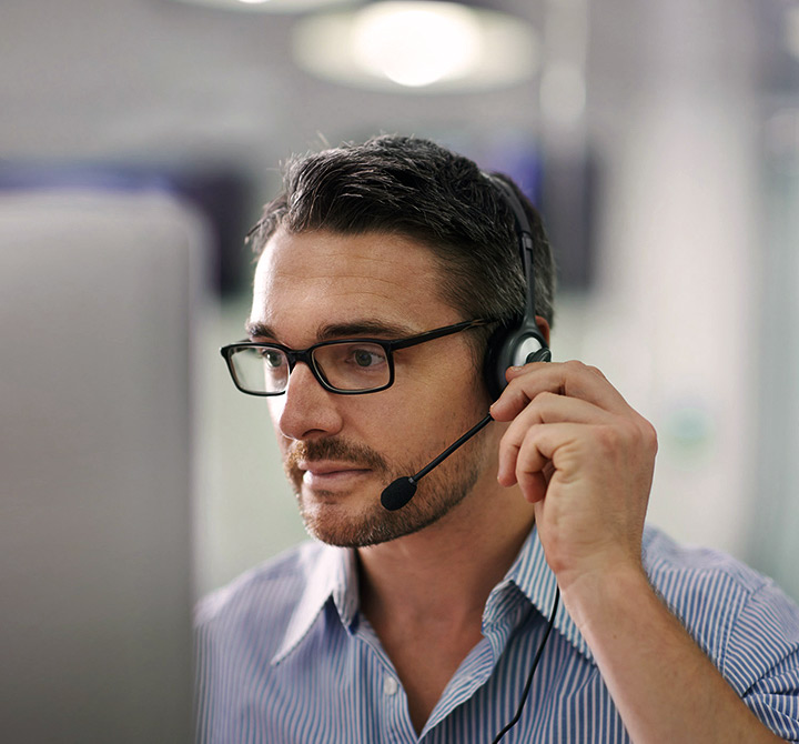 A team member is sitting at a desk wearing a headset and looking at a computer monitor to perform their business tasks.