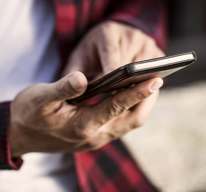 Man in a white shirt and red and black flannel shirt working on a smartphone.