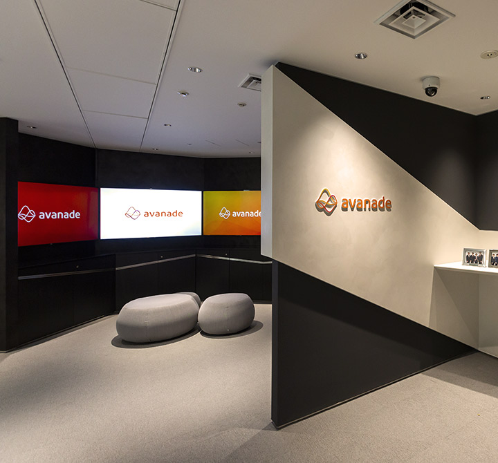 A showroom displaying three monitors with the Avanade logo, four framed pictures of executives and awards.