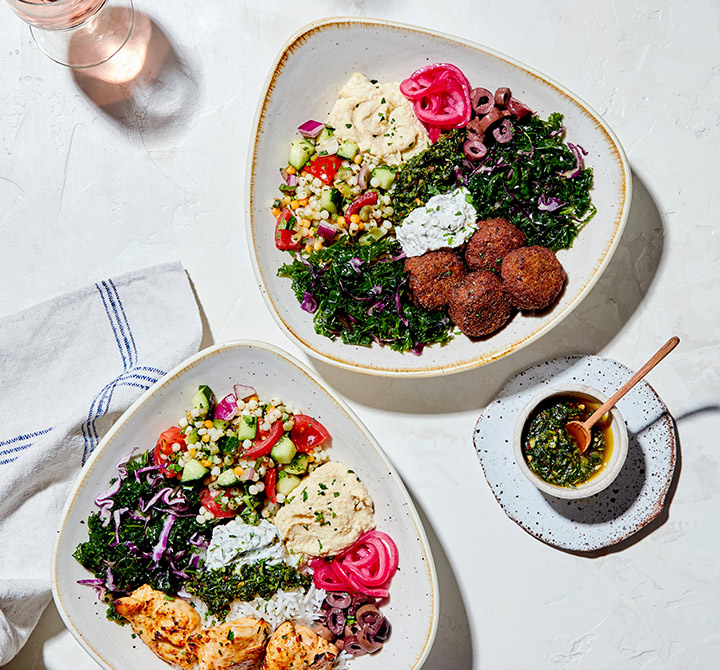 Aerial view of two white plates with gold trim full of food, three glasses, small cup saucer and a napkin on a white table.