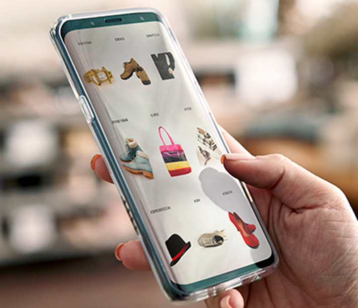 A close-up view of a female hand holding a mobile device in the vertical position displaying shopping categories.