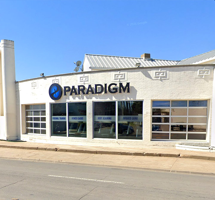 The outside view of the Paradigm Gym in Dallas, Texas; a white one level building with tall glass windows.