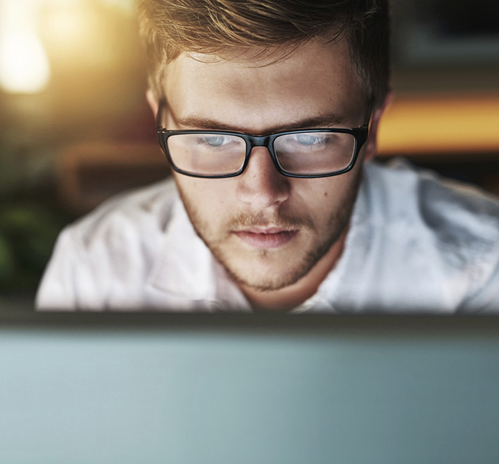 Man with glasses staring at his computer screen. 