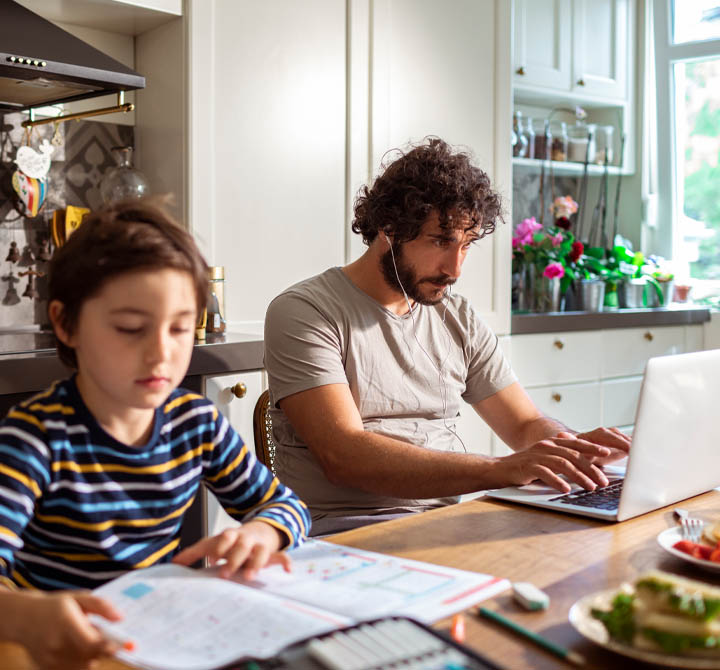 Man working at home on laptop next to child.