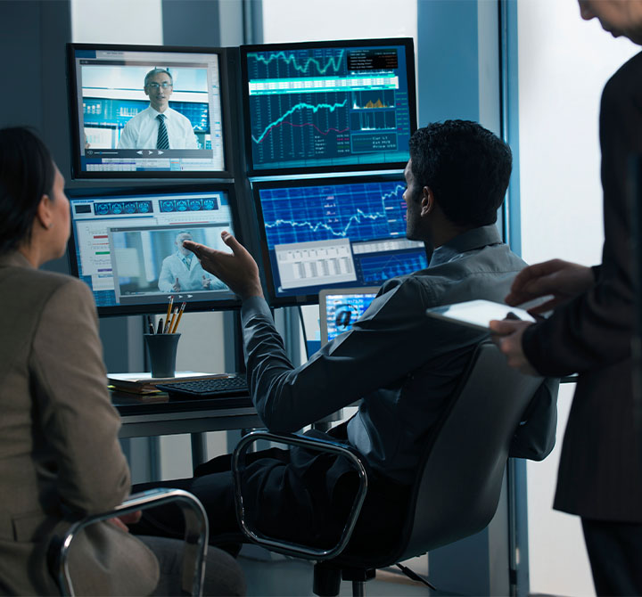 People having a discussion while looking at multiple computer monitors.