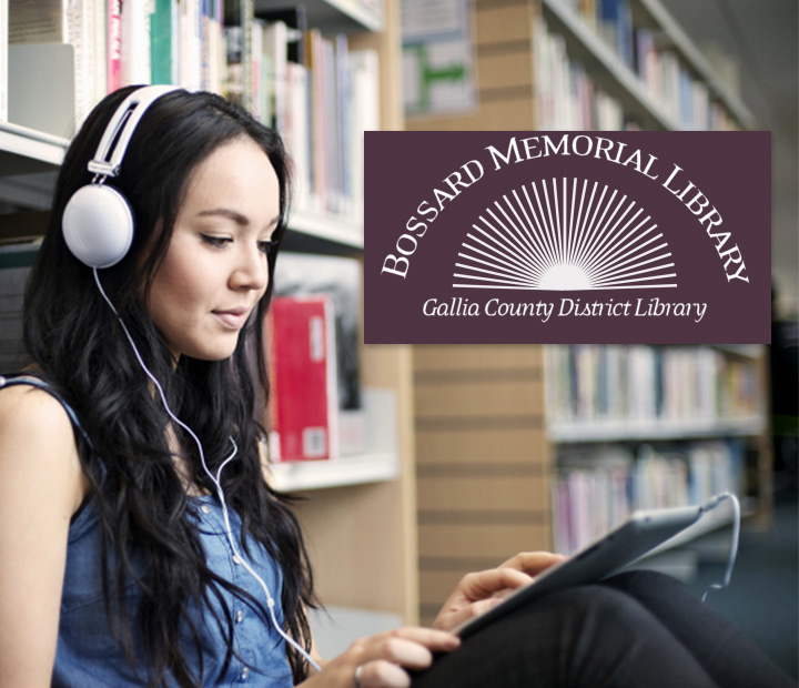 A woman wearing white headphones is sitting on the floor in a library working on her tablet..