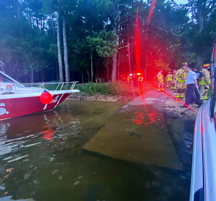 Closeup view of a TowBoatUS boat and another boat parked on the shoreline with fire fighters, paramedics in the background.