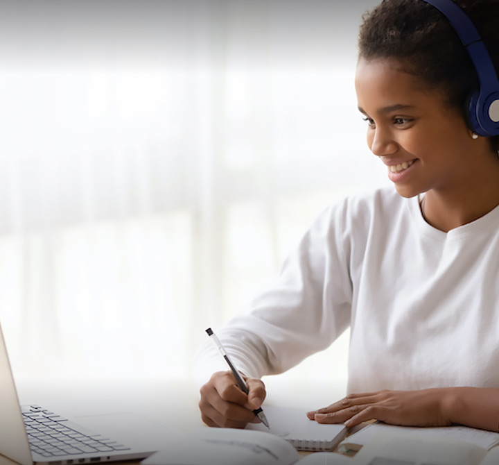 A female student, wearing a blue headset, is using a laptop computer with AT&T Fiber for a virtual teaching lesson.