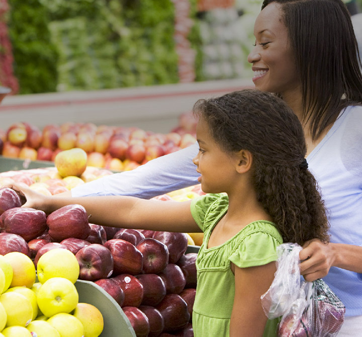 A woman and young girl are picking out red delicious apples in the produce section of an Presidente Supermarket.