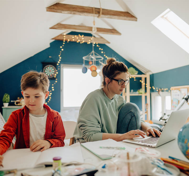Woman working on laptop from home seated next to a child.