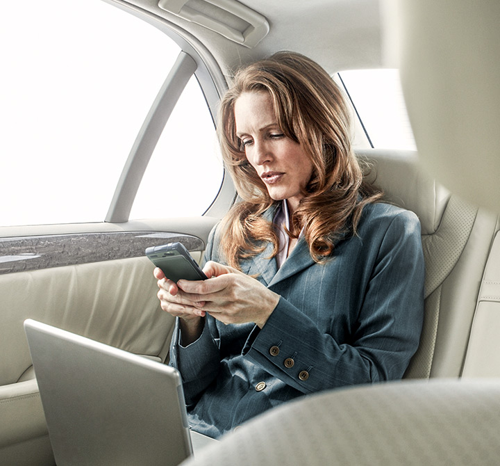 Woman in back of car using her laptop and smartphone. 