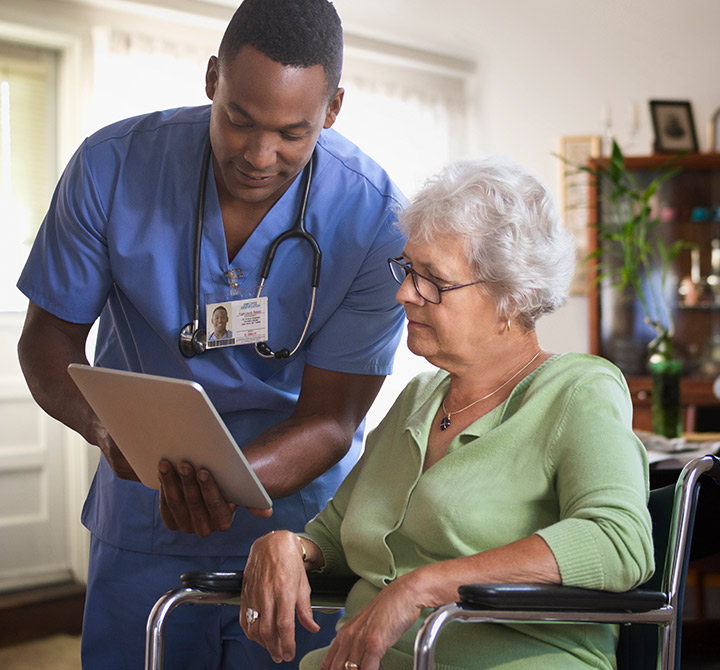 A healthcare worker holding a tablet discussing health information with older woman in wheelchair. 