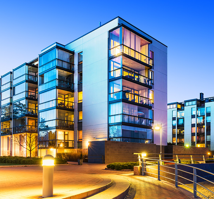 Modern hotel at dusk with street lamps and large glass windows.