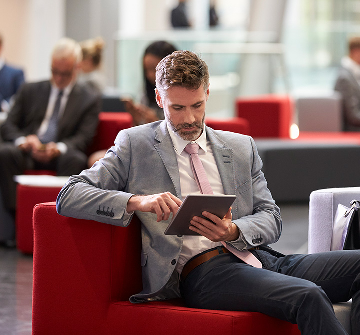 Business man in grey suite sitting in a lounge and working flexible on tablet device designed for productivity