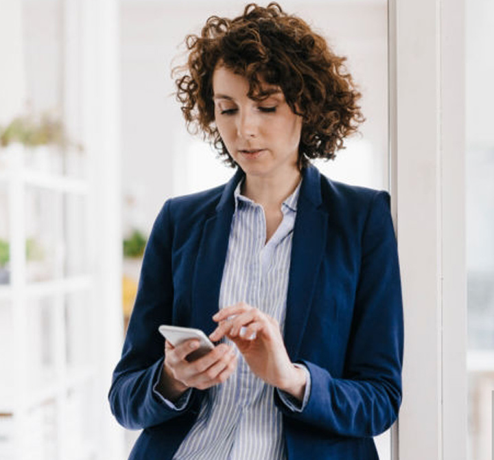 Corporate woman in blue jacket operating mobile device at work