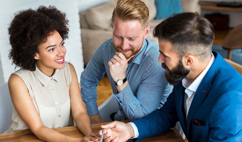 A male loan officer in a blue suit is going through loan details with a man and woman.