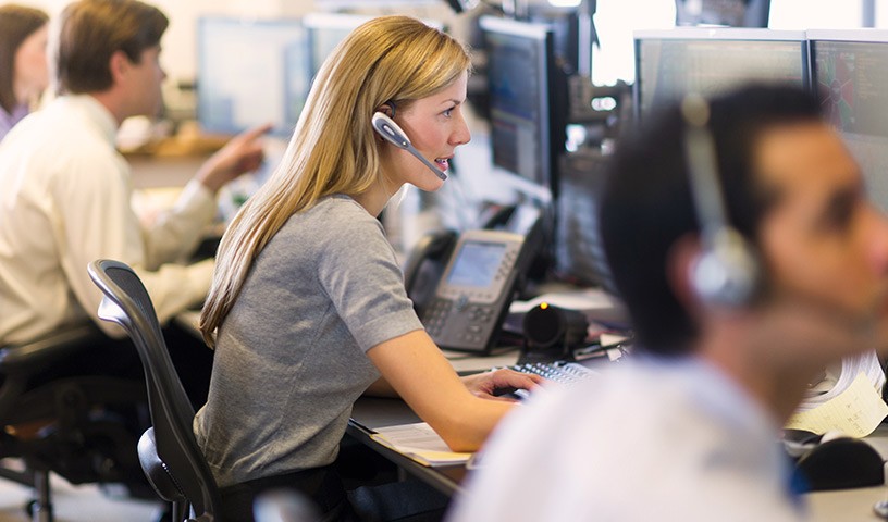 Call center representatives with headsets sitting at desk with computer monitors