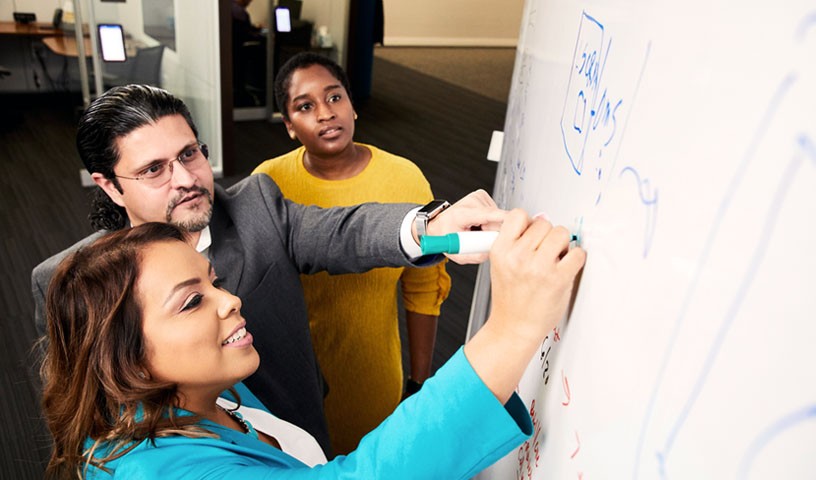 Two women and a man are having a sketch meeting on a white board.