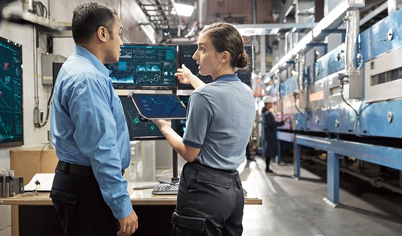 Woman showing a man internal diagnostics of a machine in a factory setting.