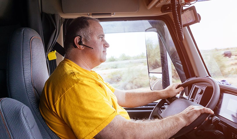 Man with yellow shirt driving with an earpiece 